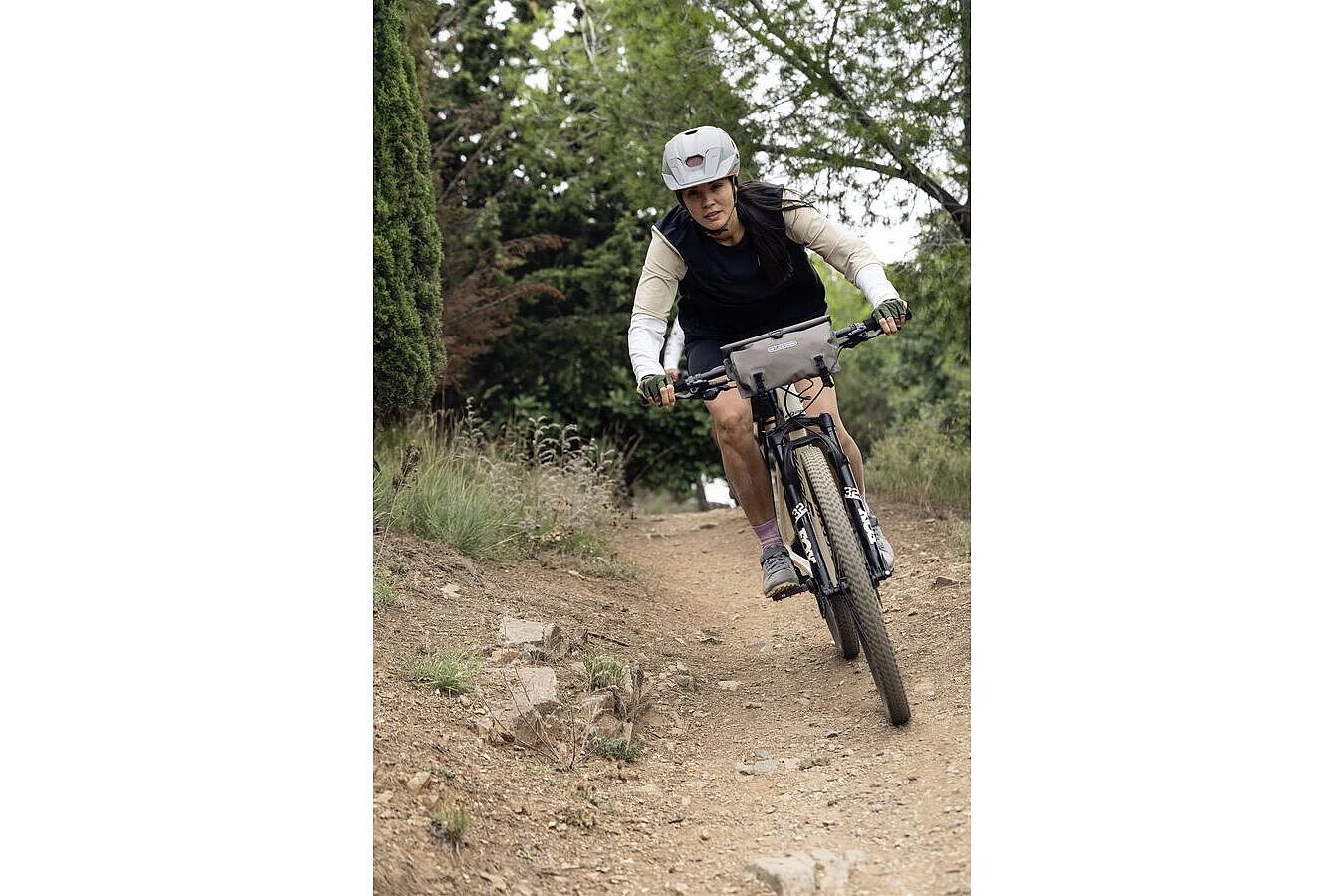 Ortlieb 2 Person fährt mit einem Mountainbike über einen schmalen, steinigen Waldweg, eine Lenkertasche am Lenker.