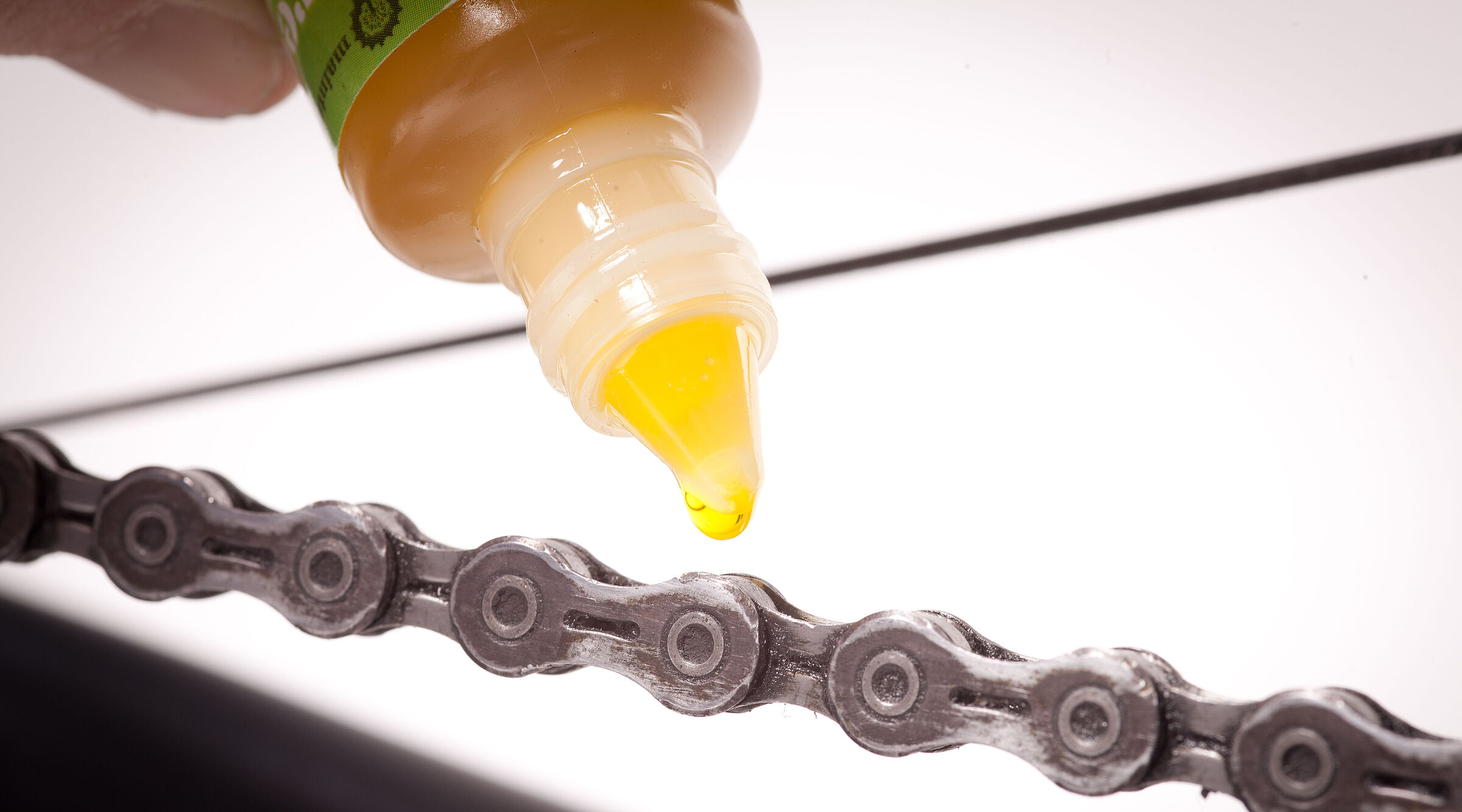 Großaufnahme eines Ölfläschchens, das an eine Fahrradkette gehalten wird. 
