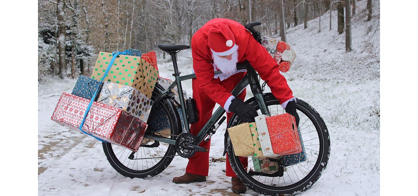 Weihnachtsmann Man in Weihnachtskleidung beugt sich über ein mit Geschenken beladenes Fahrrad im Schnee.
