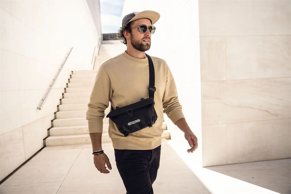 Ortlieb Eine Person trägt eine schwarze Umhängetasche und geht eine helle Treppe hinunter.